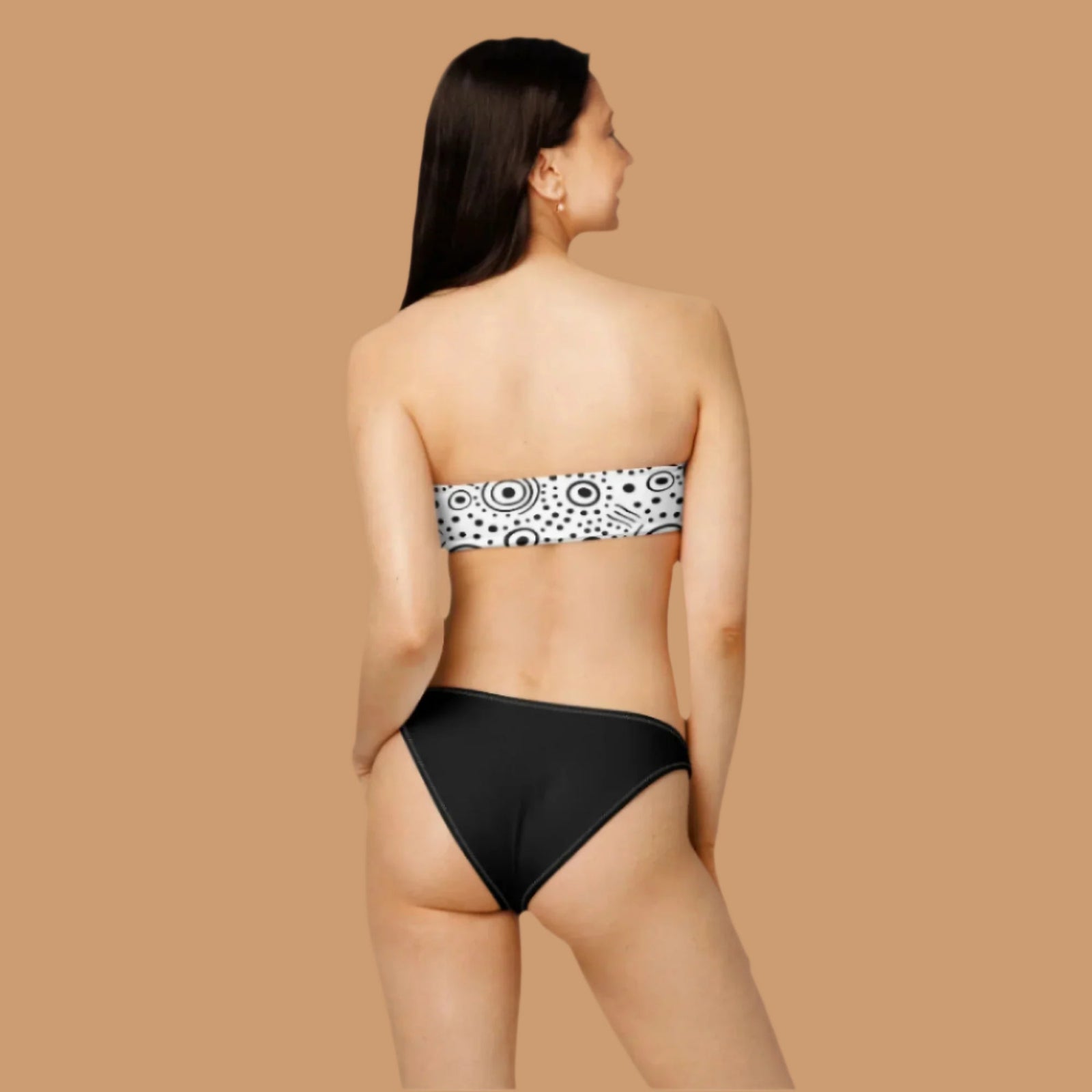 Woman wearing a black and white polka dot bandeau top and black high-waisted bikini bottom.