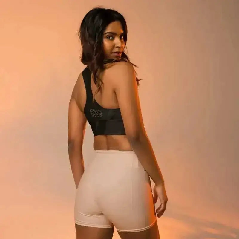 Woman showcasing a black longline sports bra and beige high-waisted shorts from behind