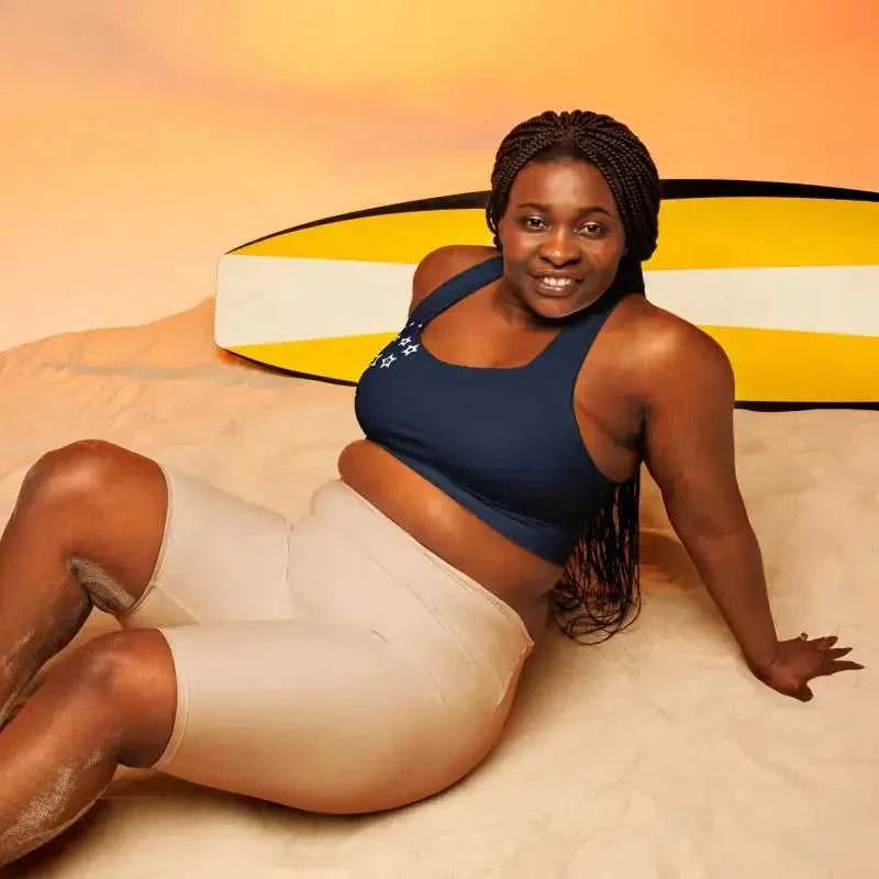 Person relaxing in Navy Recycled Longline Sports Bra with yellow surfboard behind, perfect plus size activewear