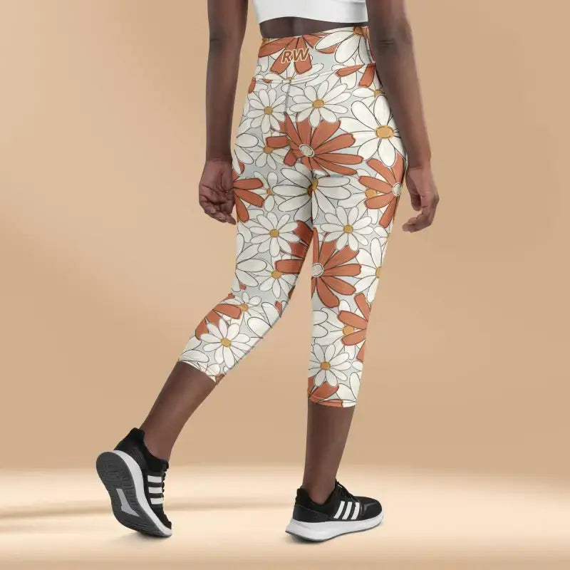 Floral print capri leggings with orange and white daisy pattern paired with black athletic shoes.