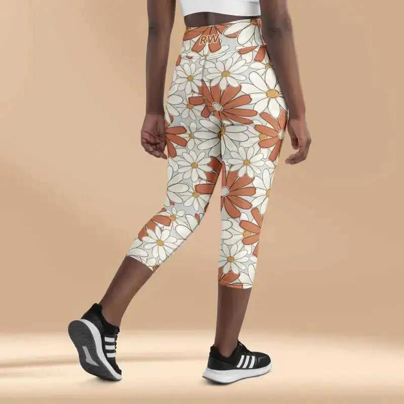 Floral print capri leggings with orange and white daisy pattern paired with black athletic shoes.