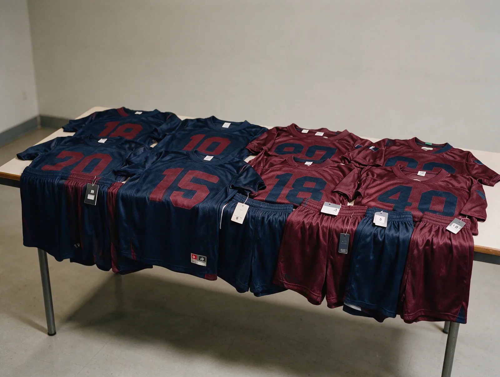 Matching navy and maroon team sports uniforms with numbered jerseys laid out by size